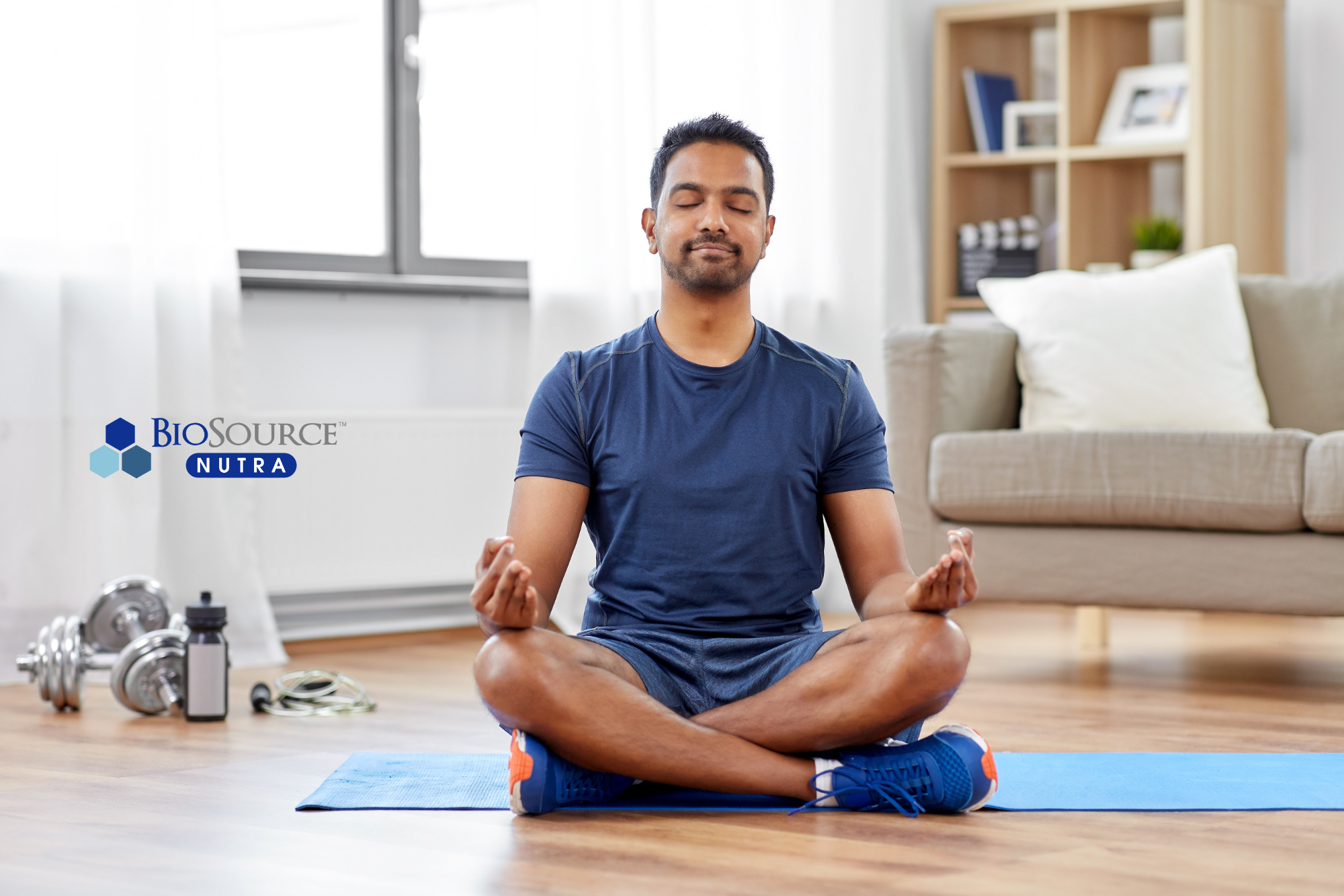 A young man sits on a yoga mat with his legs crossed meditating