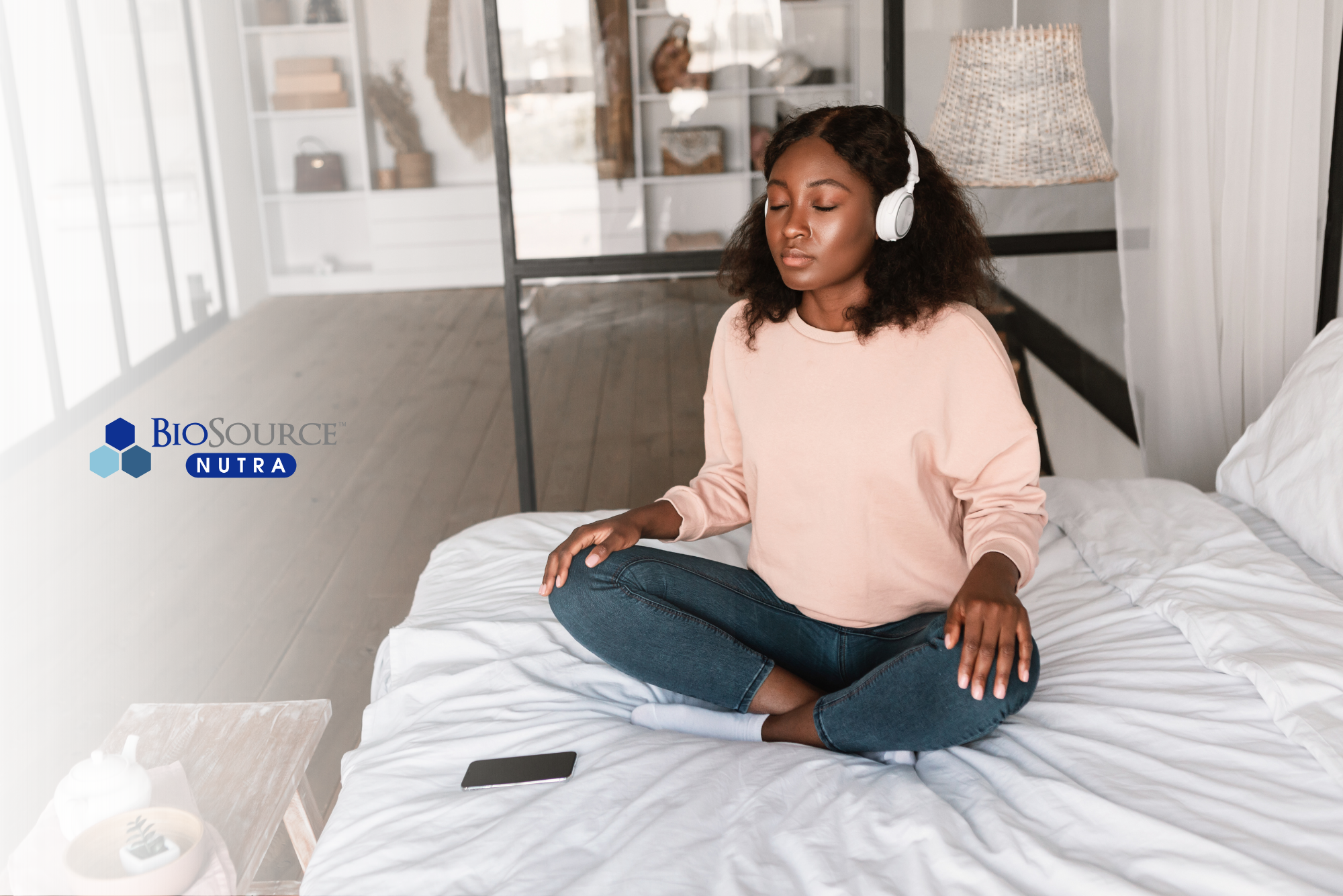 A young woman sits cross-legged on her bed and listens to a guided meditation on her phone