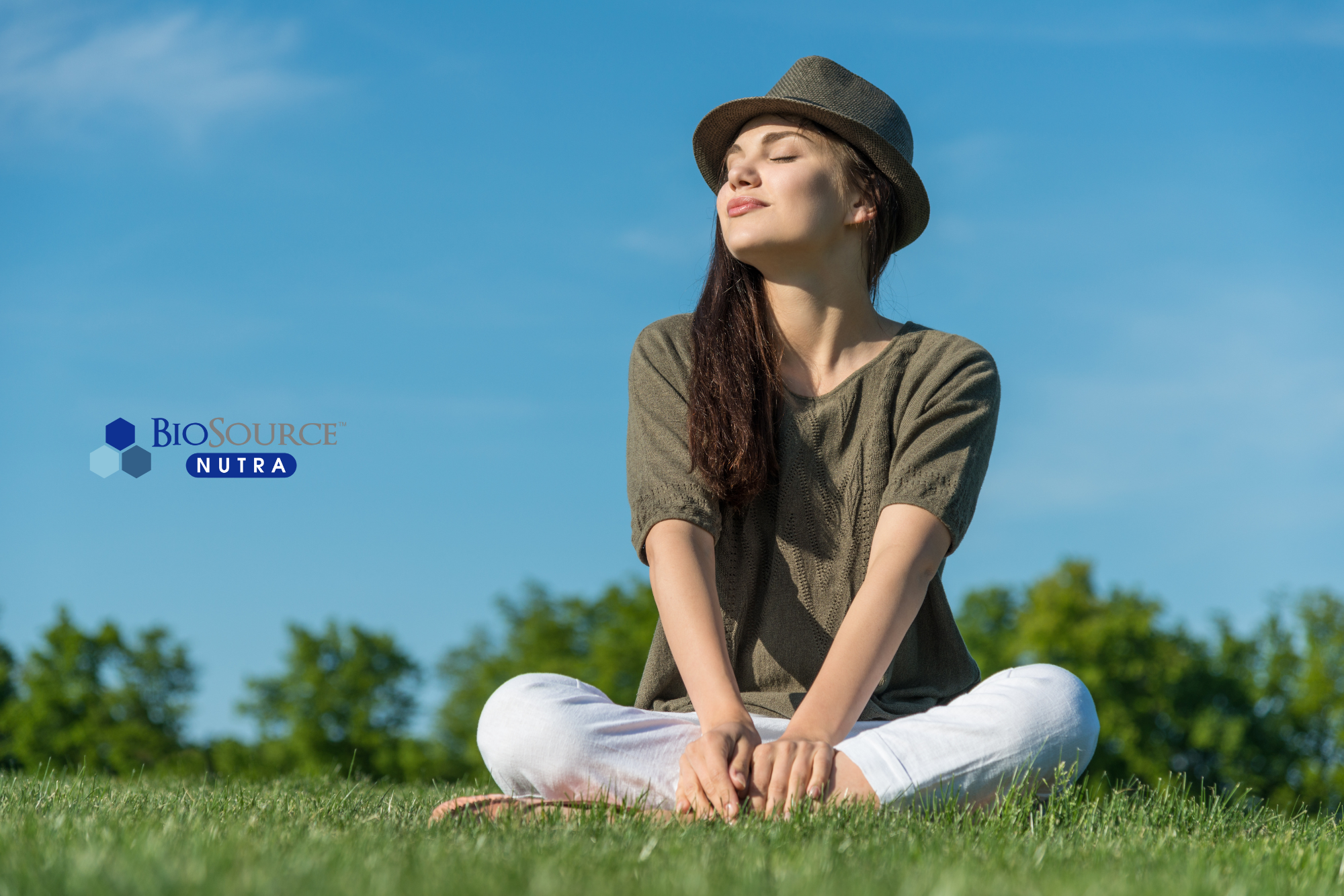 A young woman sits cross legged outside in the sunshine