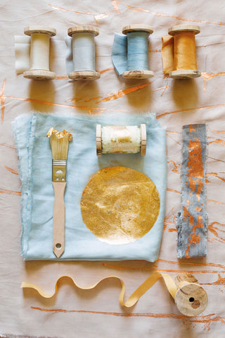 Plant dyed silk ribbons with gold leaf sun on textiles, displayed on wooden spools with paintbrush