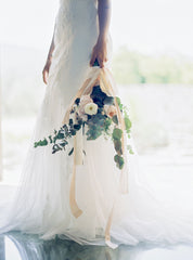 Model wearing white wedding gown holding bridal bouquet with flowing silk ribbons