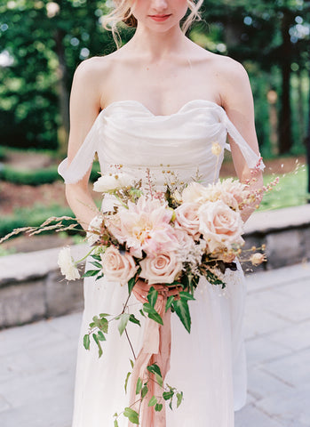 Model in bride dress holding bouqeut of pink roses tied with soft blush pink ribbon