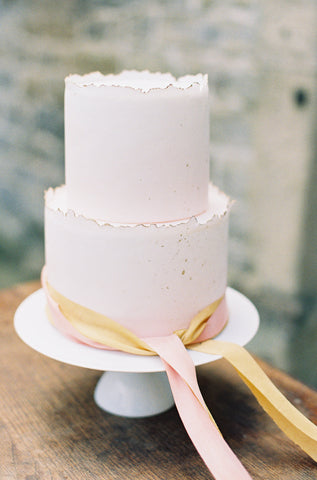 White two tier wedding cake tied with soft gold taupe and pale peach silk ribbons