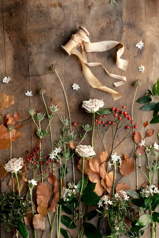 Gold and ivory silks ribbons on wooden spool with flowers and foliage to make a bouquet