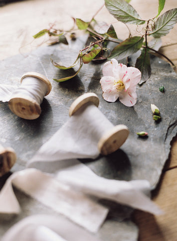 Two spools of plant dyed silk ribbon in shades of pale pink and grey displayed on table