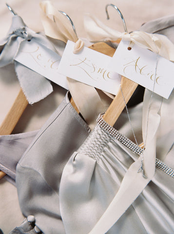 4 wooden dress hangers tied with grey and ivory silk ribbons and hung with silver necklaces and charms
