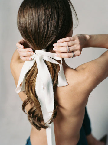 Back of models hair with silk ribbon tied in a bow at base of a low pony tail