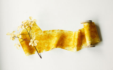 Yellow silk ribbon unwound from a wooden spoolwith foliage
