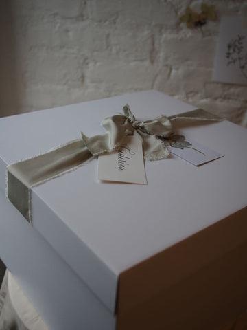 Green silk ribbon tied around a white box hamper