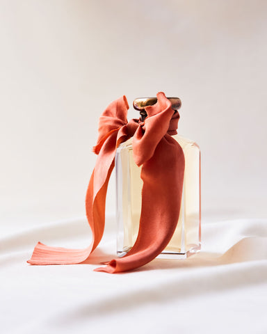 Orange silk ribbon tied in a bow wrapped around the neck of a vintage perfume bottle