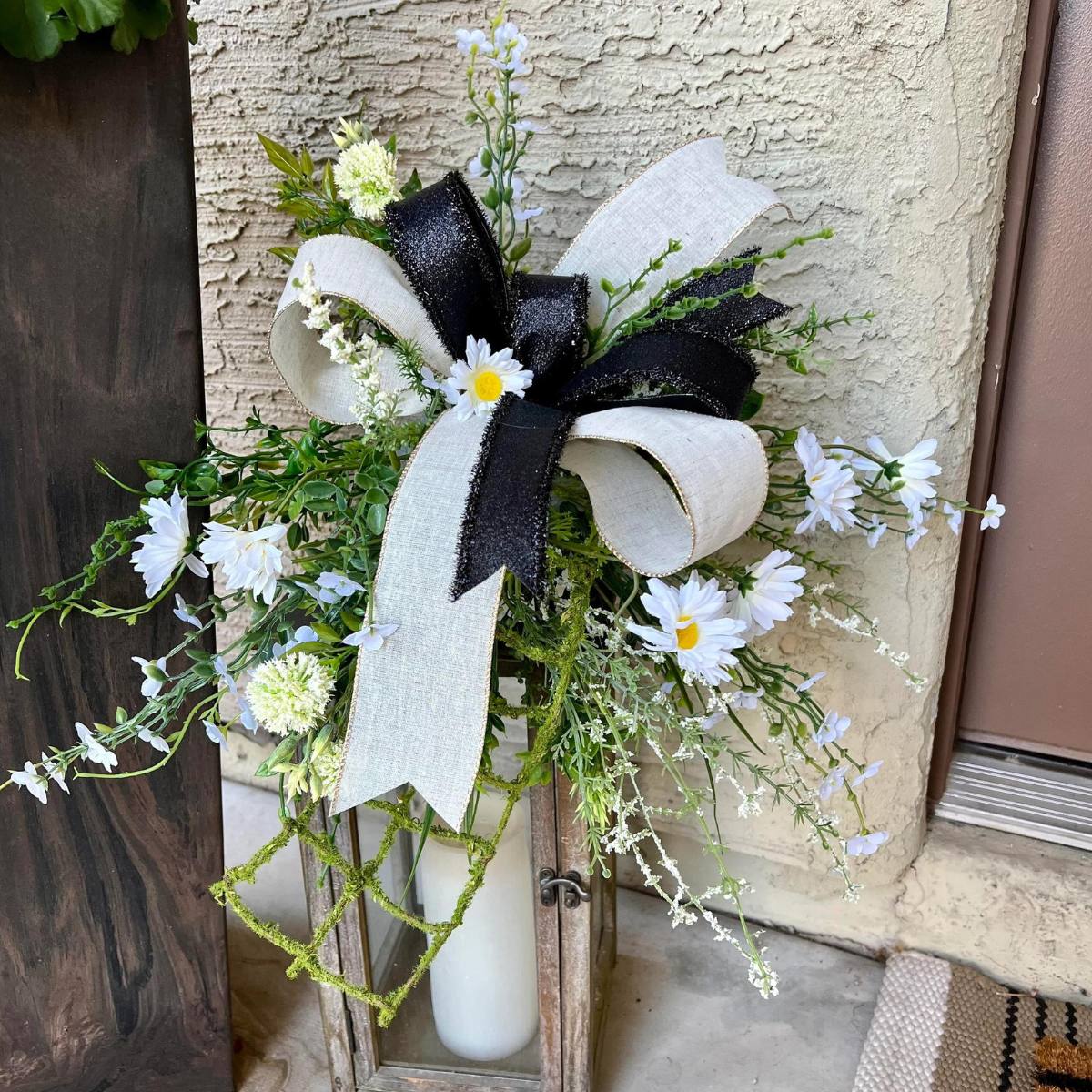 lantern topper bow with greenery, cream blooms, black and cream ribbon.