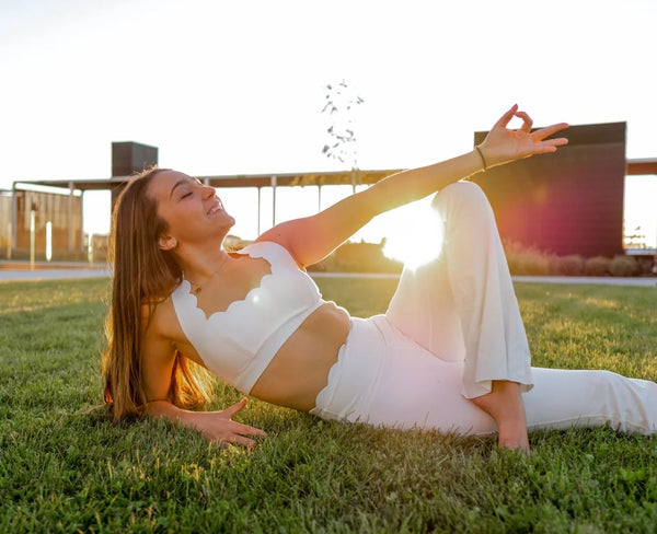 The model is wearing a comfortable white sports bra as she lies on the grass, enjoying the sunshine.