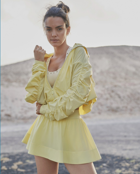 A woman is wearing a loose yellow sun-protective jacket outdoors.