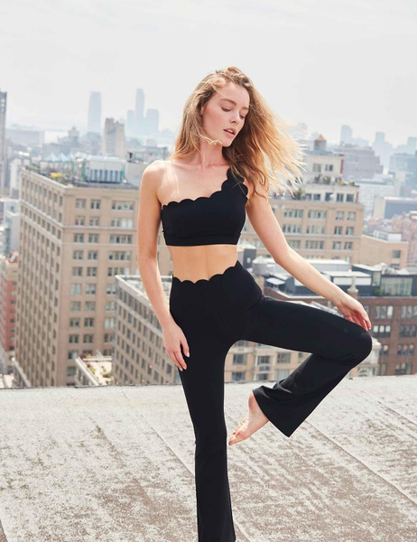 A model showcasing a black sports tank top paired with black high-waist flare leggings workout pants on the rooftop.