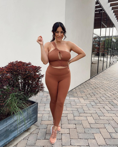 The model is showcasing a terracotta-colored sportswear set in front of a white wall.