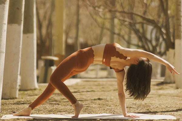 The model is wearing terracotta-colored yoga attire while practicing yoga in a peaceful forest.