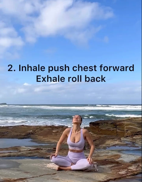 A model wearing a purple WISKII yoga set practicing SEATED CAT-COW POSE by the seaside.