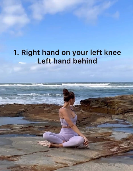 A model wearing a purple WISKII yoga set practicing SEATED SPINAL TWIST by the seaside.