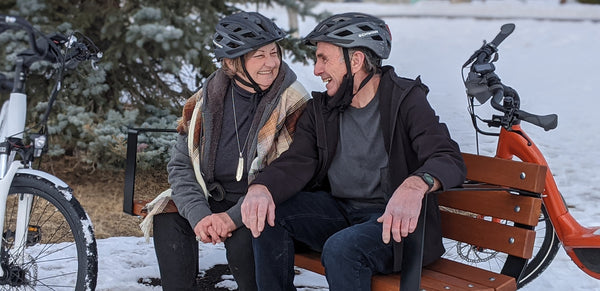 Happy couple sitting on a bench with their eBikes behind them
