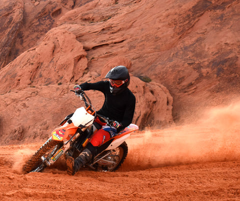 A guy riding a ktm dirt bike in the red sand in southern Utah.