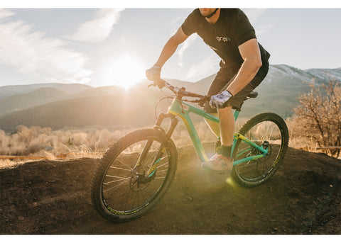 A guy wearing Gripit Gloves riding a mountain bike with a mountain sunset in the background.