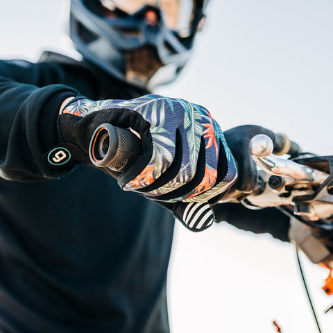 A close up of a dirt bike rider's hand gripping the handlebar while wearing the Bird of Paradise Gripit glove.