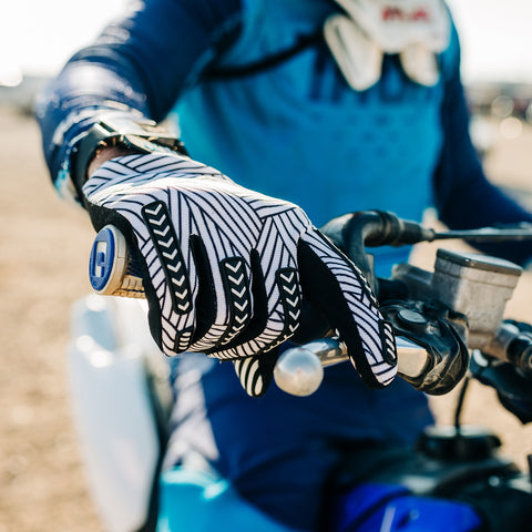 A motocross rider grabbing the bars of his dirt bike while wearing a black and white striped Gripit glove.
