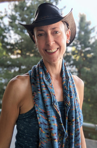 Person wearing a cowboy hat with a rainbow shawl around there neck