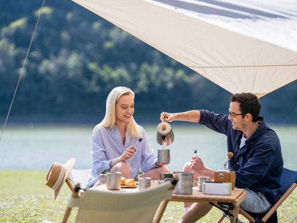A man and woman sitting under a canopy while enjoying tea and pastries together, and holding a RELX vape device in their hands. 