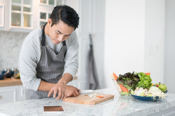  A man reading his tablet with a pensive thoughtful look while standing in his kitchen preparing a meal from a variety of fresh vegetables on the counter 