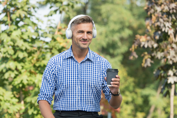 A man holding coffee and wearing headphones