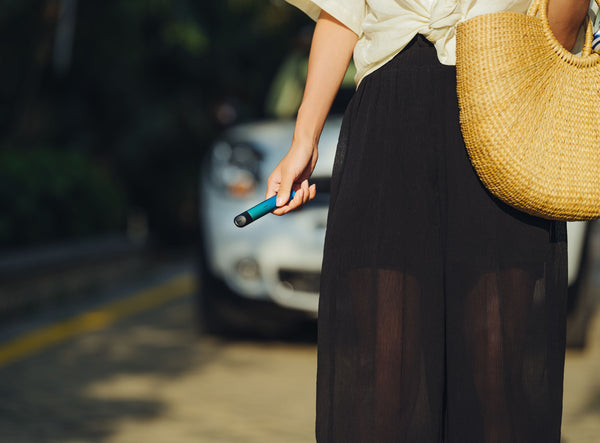 A woman in casual wear holding a blue RELX vape device in her right hand as she walks down a street.