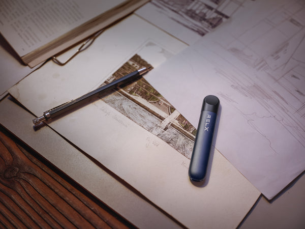 A black RELX Infinity vape device beside a pencil on a table full of papers and files.