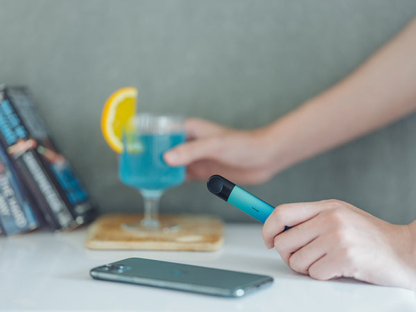Man holding a glass of a blue coloured beverage in his right hand and a RELX vape device in his left.
