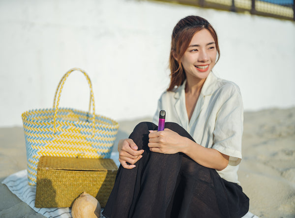 A smiling woman sitting on a mat as she holds a RELX vape device in her left hand. 