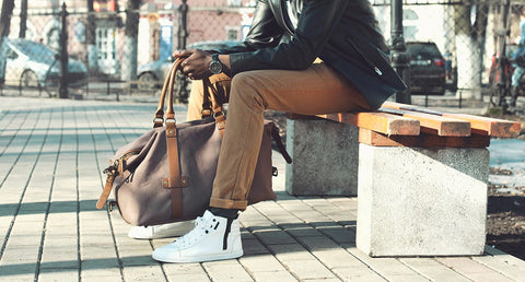 A stylish man sits on a bench in an outdoor park.