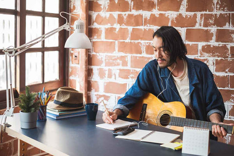 Man holding a guitar and writing songs against a brick background wall