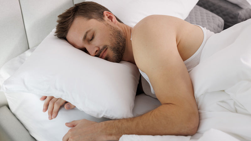 Photo of a male sleeper with his arm in the Comfort Channel of the SONU mattress and head on a top pillow with white sheets and pillowcase