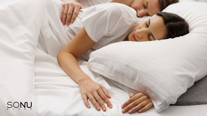 A photo of a male and female comfortably cuddling in a Sonu mattress with white sheets.