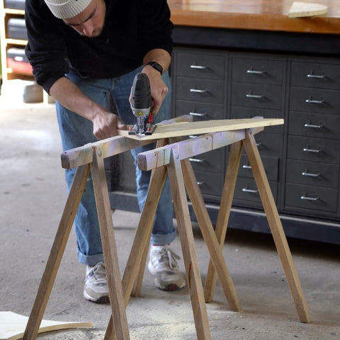 Eine Person baut auf zwei Böcken in der Werkstatt und sägt eine Platte. 