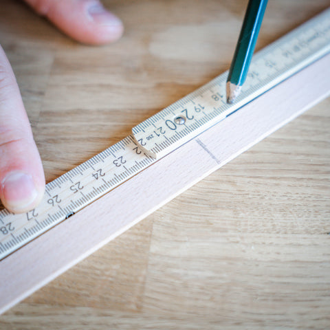 Eine Person markiert auf einer Holzleiste 20cm mit einem Zollstock und Bleistift. 