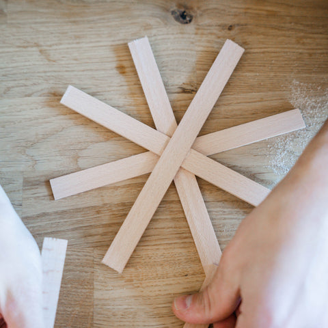 Auf einem Holztisch liegt ein Stern aus gleich langen Holzleisten. 