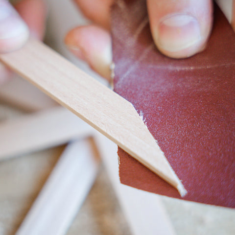 Ein abgesägtes Stück Holzleiste wird mit Hilfe von einem Schleifpapier abgeschliffen. 