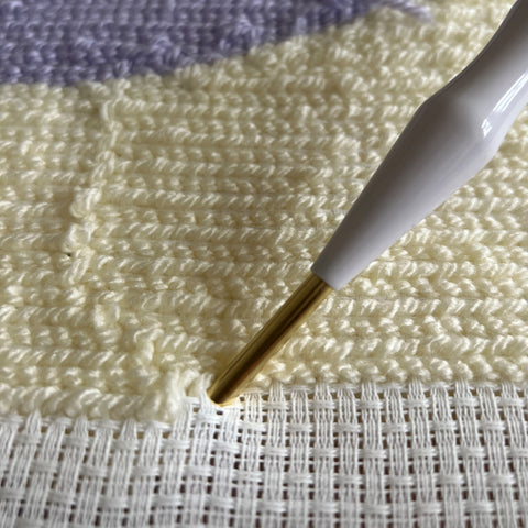 Mit einer Punch Needle Nadel wird mit einer hellen Wolle eine große Fläche gestickt. 