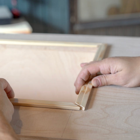 An einem Holzkasten werden Holzleisten auf Gehrung mit einem Holzleim befestigt. 