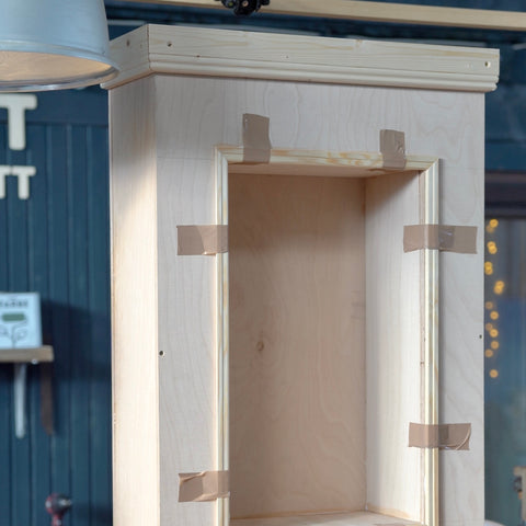 Ein Kaminssims aus Holz steht auf einer Werkbank in einer Werkstatt und die Leisten werden mit Klebeband befestigt.