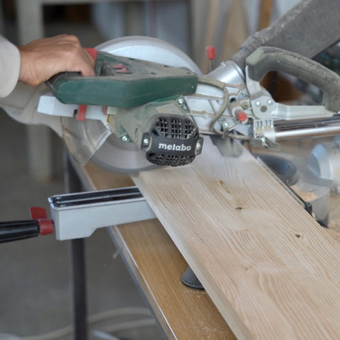 Mit einer Kappsäge wird auf einer Werkbank eine Holzplatte durchgesägt.