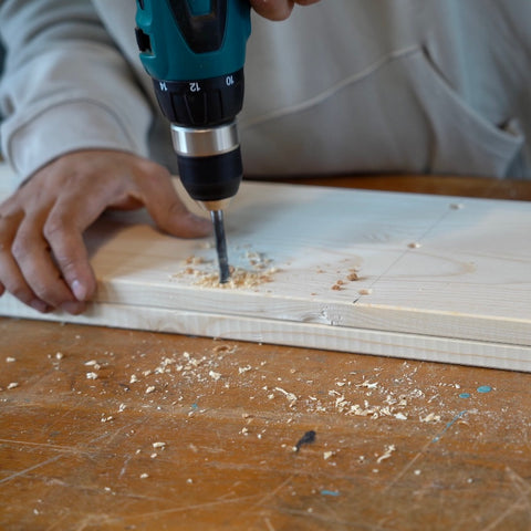 Eine Detailaufnahme zeigt, wie mit einem Holzbohrer durch zwei Holzplatten gebohrt wird. 