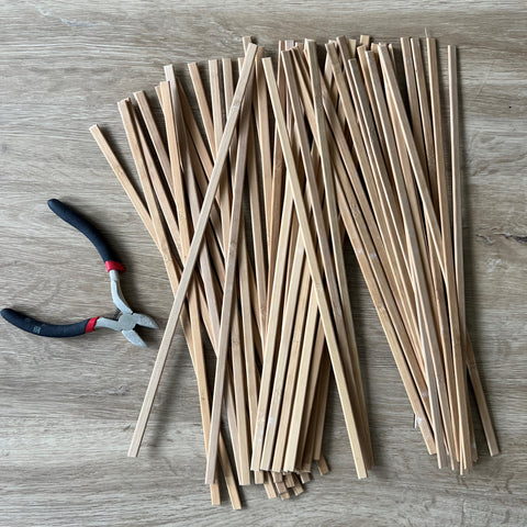 Sehr viele, dünne Holzleisten sind in der gleichen Länge zugeschnitten und liegen auf einer Holzplatte. Daneben befindet sich eine Zange. 