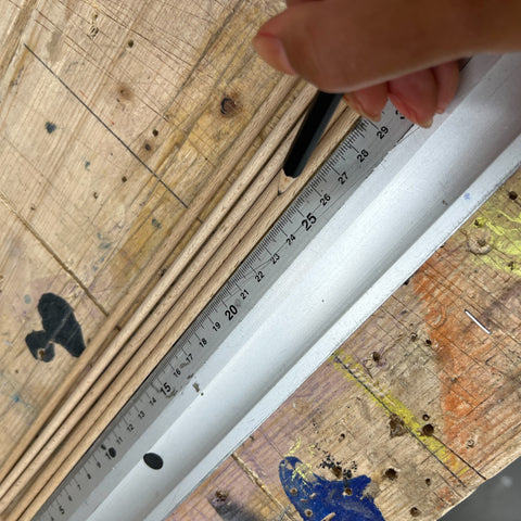 Mit einem Lineal werden dünne Holzstäbe auf eine Länge abgemessen. Eine Person markiert die Stellen mit einem Bleistift. 